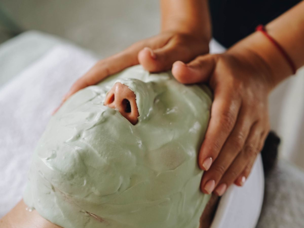 Un masque aux algues appliqué sur le visage, les mains de la praticienne au travail